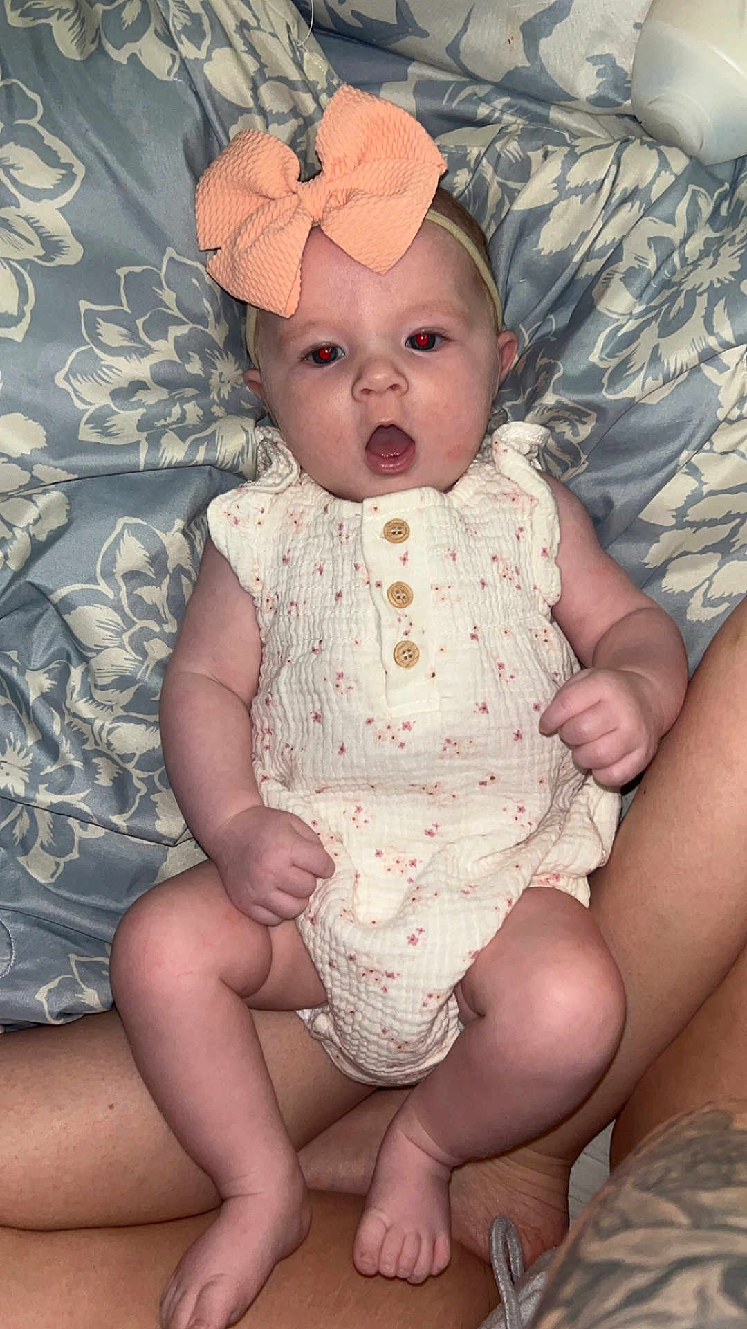 Josetta is registered to the contest to win money with this photo: baby, child, infant, bow, headband, sitting, legs, arms, clothing, onesie, person, skin, hand, foot, fabric, pattern, floral, bed, comfort, surprise