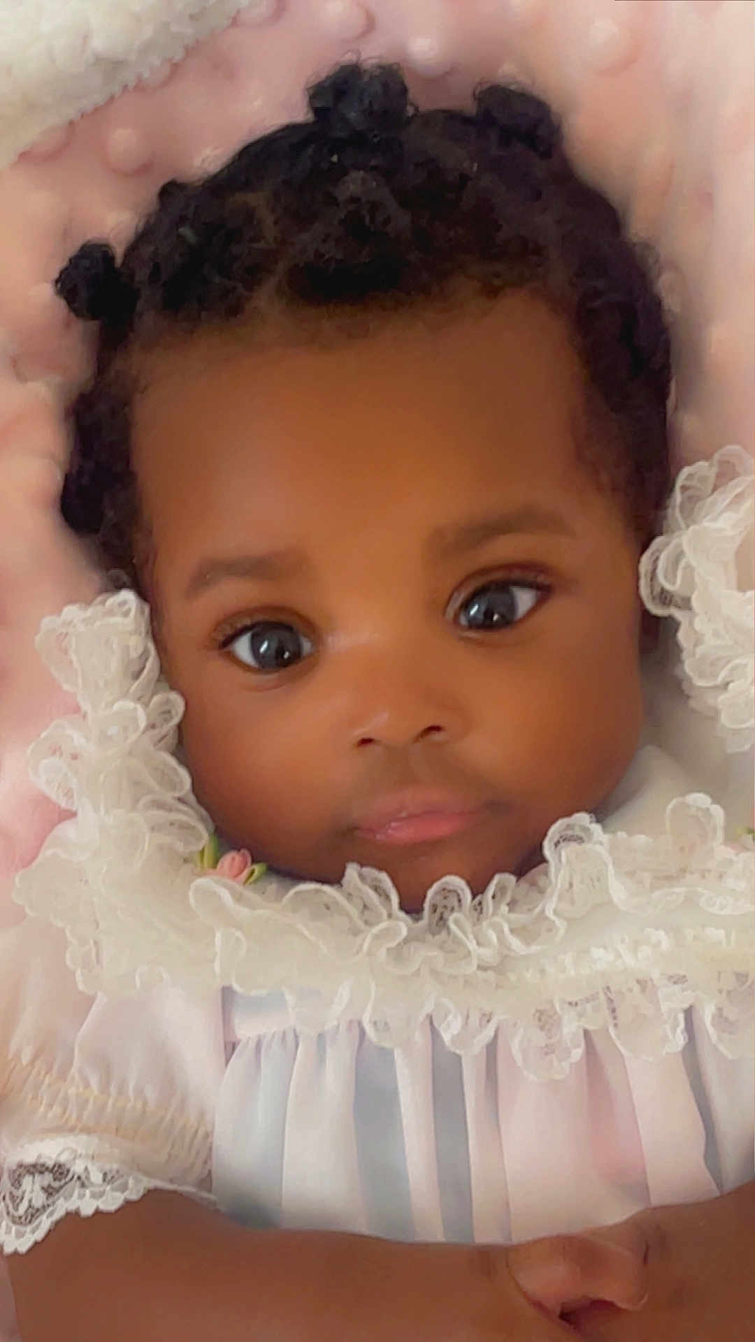 Jaminah joined the competition — help win amazing prizes! baby, infant, close_up, portrait, face, hands, clothing, white_dress, lace, frills, curly_hair, black_hair, big_eyes, cute, soft, pink_background, newborn, adorable, child, indoor