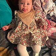 Aveah is registered to the contest to win money with this photo: baby, infant, sticking_tongue, floral_dress, bib, headband, blanket, pillow, tights, shoes, smile, wide_eyes, portrait, indoor, cozy, fabric_pattern, sofa, cute, hands, legs
