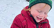 Kingslyn Kole is registered to the contest to win money with this photo: child, toddler, winter_clothing, red_jacket, green_hat, snow, outdoor, laughing, happy, playful, snowflakes, cold_weather, smiling, cute, face, portrait, nature, trees, daytime, fun