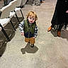 Kingslyn Kole is registered to the contest to win money with this photo: toddler, child, indoor, person, red_hair, vest, plaid_shirt, brown_pants, shoes, folding_chairs, adults, shadow, walking, concrete_floor, event, people, standing, casual, clothing, curious