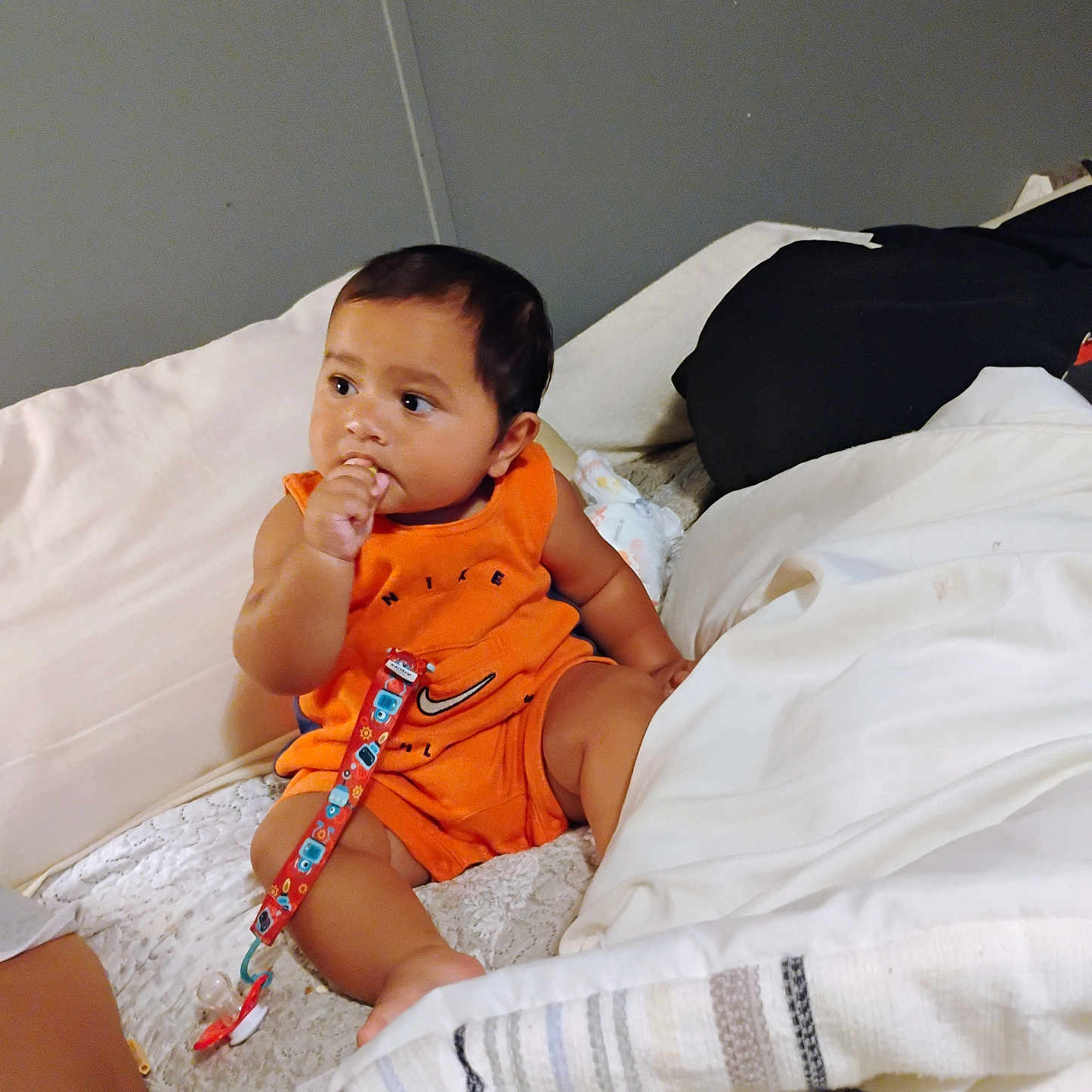 Taiyln is registered to the contest to win money with this photo: baby, bed, blanket, child, comfort, cute, face, hair, indoors, infant, orange_clothing, pacifier_clip, person, pillow, relaxed, rest, sitting, skin, thumb_in_mouth, young