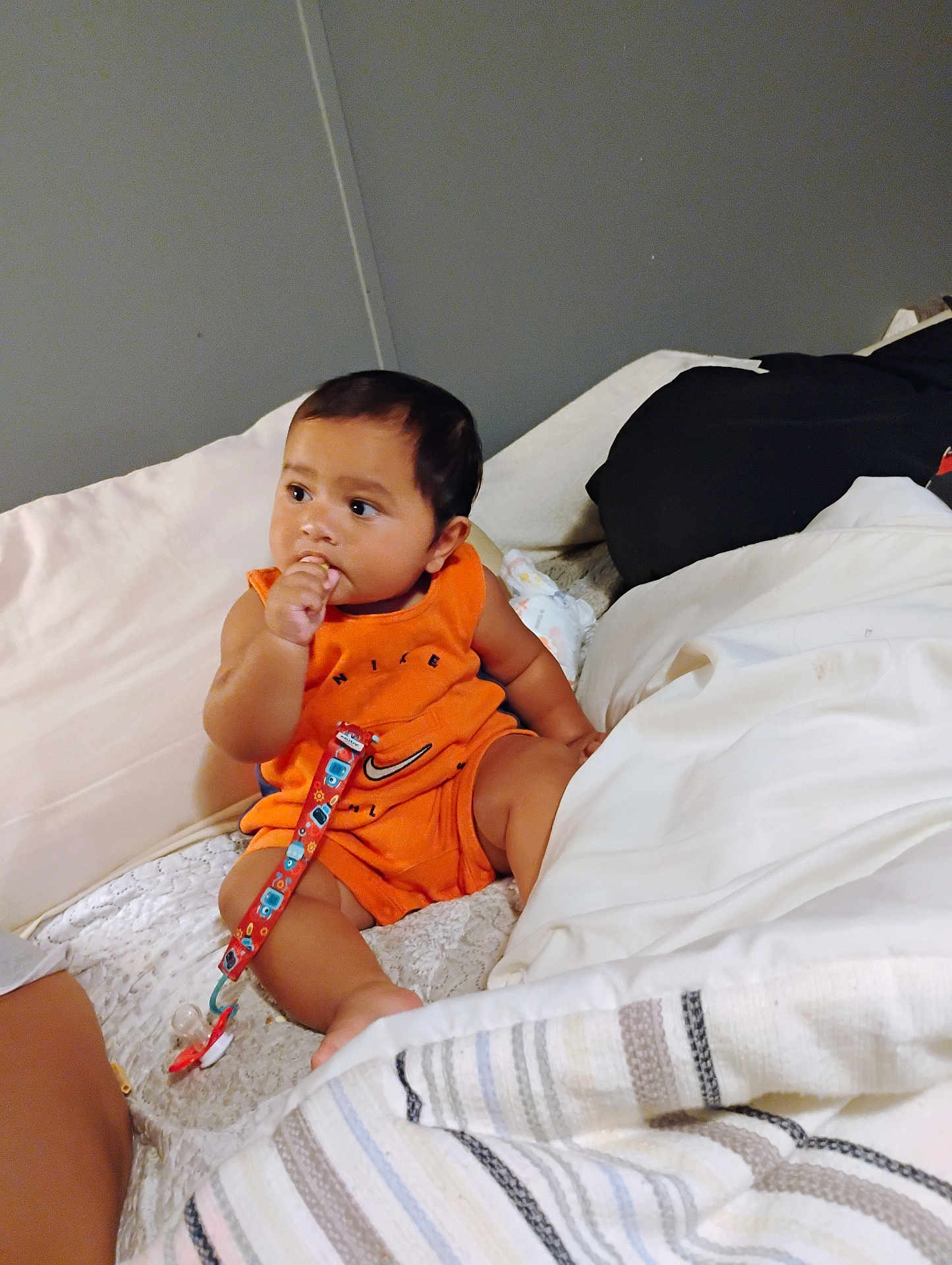 Taiyln is registered to the contest to win money with this photo: baby, child, infant, orange_clothing, bed, blanket, pillow, indoors, person, sitting, thumb_in_mouth, cute, young, face, hair, skin, pacifier_clip, comfort, rest, relaxed