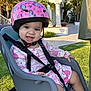 child, clothing, cute, daytime, grass, happy, hello_kitty, helmet, outdoor, person, pink, playful, safety, seatbelt, smile, stroller, suburban, sunlight, toddler, unicorn