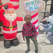 Nathaniel is registered to the contest to win money with this photo: child, boy, inflatable, santa_claus, candy_cane, north_pole, holiday, indoor, festive, plush, floor, wall, smiling, clothing, red, green, toy, decoration, person, celebration