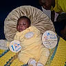 baby, child, yellow_clothing, pillow, blanket, milestone_sign, indoor, couch, sibling, curious, knitted_blanket, portrait, cute, infant, smiling, face, person, home, cozy, family