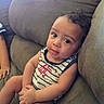 Dj is registered to the contest to win money with this photo: baby, child, couch, striped_clothing, tank_top, indoor, curly_hair, cute, portrait, seated, relaxed, furniture, infant, skin, face, hand, expression, looking_at_camera, young, casual