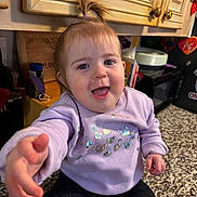 Autumn is registered to the contest to win money with this photo: toddler, child, kitchen, countertop, cabinet, purple_sweater, black_pants, smiling, happy, person, indoor, hair_ponytail, reaching_hand, face, blue_eyes, skin, furniture, household_items, closeup, casual_clothing
