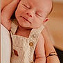baby, infant, smiling, sleeping, striped_overalls, arm, adult, closeup, portrait, soft_lighting, skin, peaceful, cute, child, newborn, hand, warm_colors, indoor, person, toddler