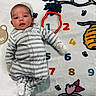 baby, infant, child, portrait, lying_down, striped_onesie, onesie, smiling, face, indoor, blanket, milestone_blanket, wooden_marker, numbers, colorful, cartoon, bees, honeycomb, cozy, photography