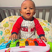 Ares joined the competition — help win amazing prizes! baby, child, infant, smiling, happy, sitting, crib, nursery, toy, keyboard, musical_toy, colorful, pajamas, red_shirt, portrait, indoor, playtime, face, hands, crib_bedding