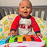 baby, child, infant, smiling, happy, sitting, crib, nursery, toy, keyboard, musical_toy, colorful, pajamas, red_shirt, portrait, indoor, playtime, face, hands, crib_bedding