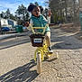 basket, bicycle, blue_sky, boots, child, daytime, girl, jackets, license_plate, outdoor, pavement, peace_sign, playful, portrait, princess, residential_area, street, training_wheels, trees, yellow_bike