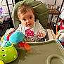 Gabriella participe au concours pour gagner de l'argent avec cette photo : baby, blurred_toy, child, clothing, curious, cute, expression, face, furniture, green_chair, hands, high_chair, household_items, indoor, person, plush_toy, shelf, sitting, toy, tray