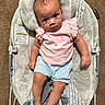 baby, infant, child, baby_rocker, pink_shirt, blue_shorts, carpet, plush_cushion, patterned_fabric, footwear, barefoot, indoor, cute, portrait, seated, looking_up, curious_expression, soft_texture, baby_clothing, small_hands