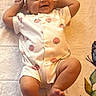 Rayne is registered to the contest to win money with this photo: baby, infant, smile, headband, flower, onesie, strawberry_pattern, blanket, butterfly, leaf, happy, cute, lying_down, relaxed, child, person, feet, arms, skin, indoors