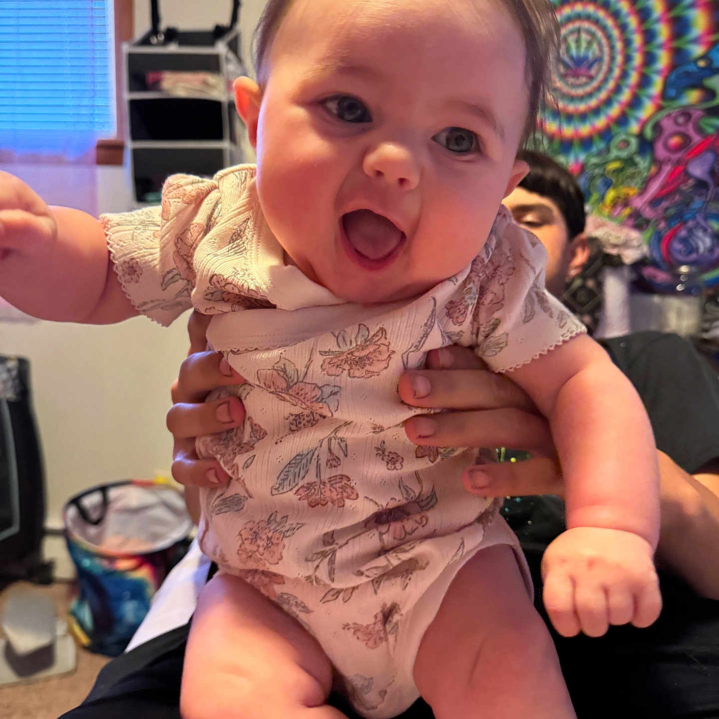 Eleigha is registered to the contest to win money with this photo: adult, baby, child, colorful, expression, face, furniture, hands, happy, holding, human, indoor, joy, patterned_clothing, person, portrait, room, smiling, tapestry, window