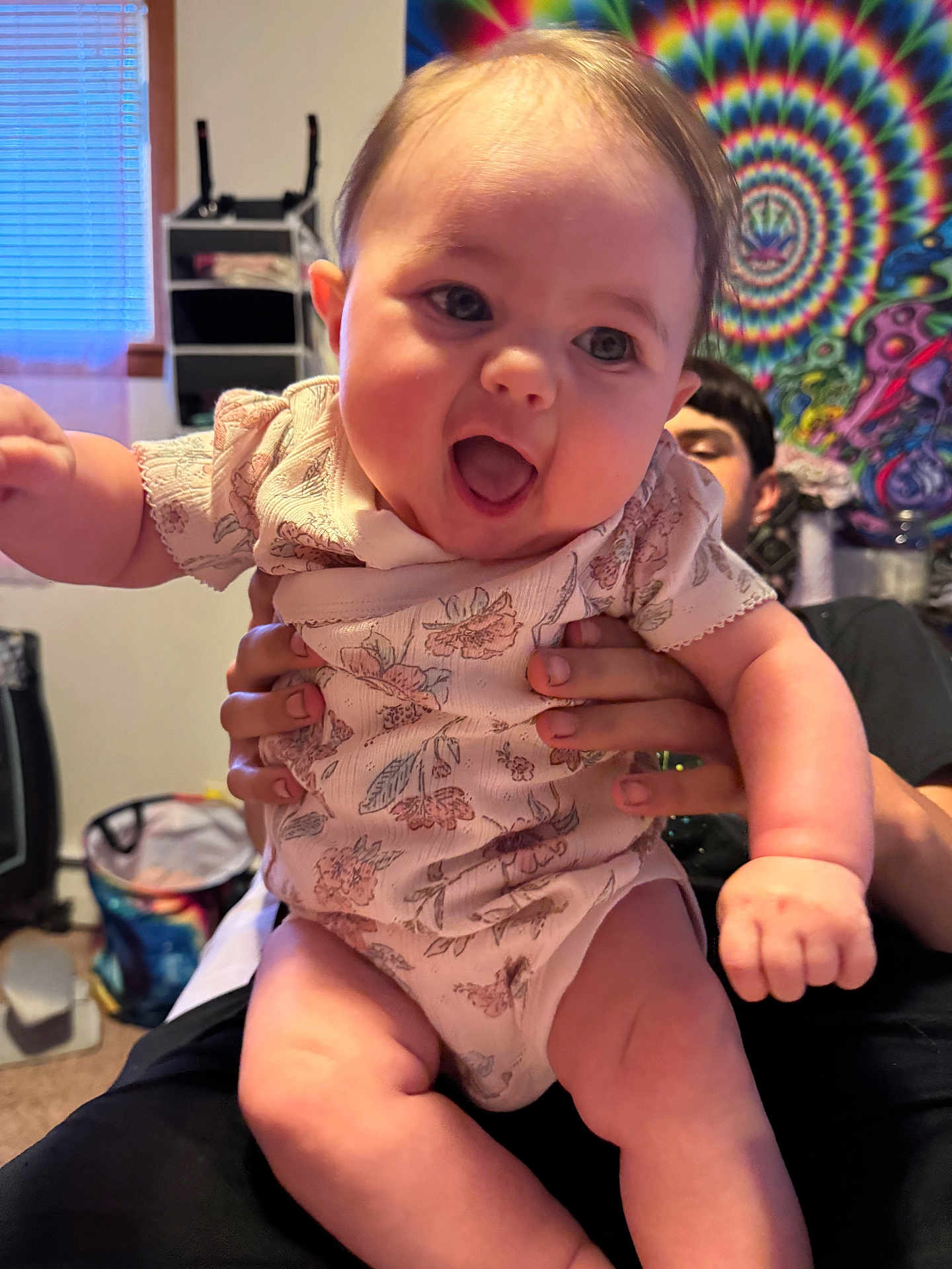 Eleigha is registered to the contest to win money with this photo: baby, child, person, smiling, happy, indoor, holding, hands, tapestry, colorful, patterned_clothing, face, human, room, window, furniture, adult, expression, joy, portrait