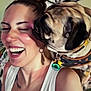 woman, dog, pug, laughing, affection, pet, indoor, smiling, face, white_shirt, earrings, tattoo, collar, tag, closeup, joy, love, interaction, friendship, hair_bun