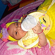 Crystal is registered to the contest to win money with this photo: baby, bottle, milk, yellow_clothing, headband, flower, blanket, infant, child, cute, lying_down, feeding, hand, pink_blanket, bed, indoors, person, sleepwear, toddler, smiling