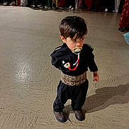 Devrane participe au concours pour gagner de l'argent avec cette photo : child, pacifier, black_clothing, patterned_belt, floor, people, costumes, group, indoor, shoes, standing, traditional_clothing, crowd, blurred_background, person, young_child, hair, face, shadow, event