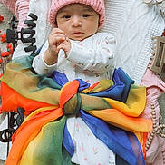 Nayra is registered to the contest to win money with this photo: baby, infant, pink_hat, pom_poms, floral_onesie, colorful_scarf, blanket, soft_toys, cute, child, indoors, portrait, smiling, cozy, warm, decorations, playful, lying_down, headwear, newborn