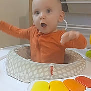 Noah joined the competition — help win amazing prizes! baby, infant, child, orange_clothing, baby_activity_center, toy_piano, indoor, storage_bins, toys, expression, motion_blur, face, head, seat, playtime, home, furniture, baby_toys, child_care, happy