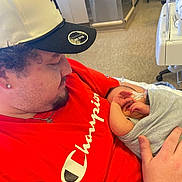 Caspian is registered to the contest to win money with this photo: newborn, baby, infant, child, father, parent, hospital, hospital_room, cuddling, family, portrait, cap, hat, red_shirt, gray_blanket, hands, sleeping, indoor, medical_equipment, birth