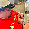 newborn, baby, infant, child, father, parent, hospital, hospital_room, cuddling, family, portrait, cap, hat, red_shirt, gray_blanket, hands, sleeping, indoor, medical_equipment, birth