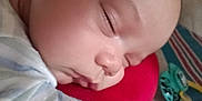 Avalon is registered to the contest to win money with this photo: baby, sleeping, close_up, face, cushion, red, blanket, striped, toy, peaceful, child, infant, resting, soft_lighting, indoors, portrait, cozy, head, person, young