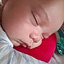baby, sleeping, close_up, face, cushion, red, blanket, striped, toy, peaceful, child, infant, resting, soft_lighting, indoors, portrait, cozy, head, person, young