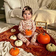 Mila joined the competition — help win amazing prizes! baby, toddler, child, pumpkin, orange, white_pumpkin, blanket, autumn, seasonal, cozy, indoor, floor, sign, clothing, pink_bow, sitting, cute, face, person, home