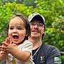 Jaxon joined the competition — help win amazing prizes! toddler, child, adult, person, smile, happy, clapping, outdoor, greenery, nature, blurred_background, casual_clothing, cap, glasses, short_sleeves, necklace, facial_hair, daylight, portrait, family