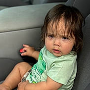 Jaxon is registered to the contest to win money with this photo: toddler, child, car_seat, seatbelt, green_shirt, camo_shorts, curly_hair, serious_expression, car_interior, gray_upholstery, small_hand, sitting, portrait, young_child, clothing, indoor, baby, person, casual, closeup