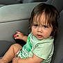 toddler, child, car_seat, seatbelt, green_shirt, camo_shorts, curly_hair, serious_expression, car_interior, gray_upholstery, small_hand, sitting, portrait, young_child, clothing, indoor, baby, person, casual, closeup