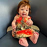baby, child, red_hair, smiling, dress, tropical_pattern, sitting, blue_chair, indoor, happy, cute, portrait, barefoot, infant, person, skin, furniture, head, expression, light