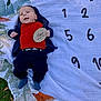 Ryker is registered to the contest to win money with this photo: baby, infant, milestone, blanket, outdoor, grass, plaque, clothing, red_shirt, navy_pants, socks, numbers, nature, child, cute, lying_down, person, smiling, hoodie, milestone_marker