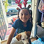 child, girl, puppy, dog, reindeer_antlers, smiling, indoors, doorway, sunlight, backpack, bottled_water, wooden_floor, neighborhood, car, tree, toy, happy, pet, casual_clothing, home