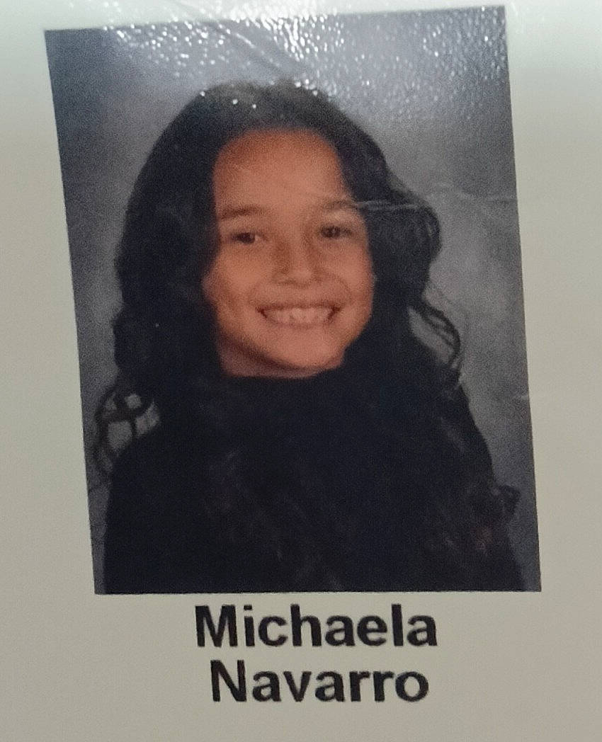 Michaela is registered to the contest to win money with this photo: background, black_top, casual, child, curly_hair, dark_clothing, face, female, glossy_photo, headshot, identity_photo, name_tag, person, portrait, print, school_photo, smiling, studio_photo, yearbook, young
