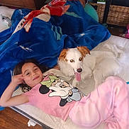 Vanessa is registered to the contest to win money with this photo: child, dog, pajamas, blanket, mattress, indoor, relaxed, smiling, sleeping, person, wood_floor, furniture, blue_blanket, pink_clothing, animal, pet, cute, happy, tongue_out, home