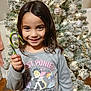 Vanessa is registered to the contest to win money with this photo: child, girl, smiling, candy_cane, christmas_tree, holiday, decorations, ornaments, lights, sweater, ponies, indoor, festive, happy, young, person, long_hair, celebration, winter, home