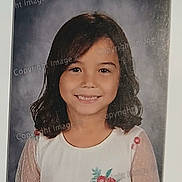 Vanessa is registered to the contest to win money with this photo: child, girl, portrait, smiling, school_photo, white_shirt, embroidered_flowers, dark_hair, shoulder_length_hair, polka_dot_sleeves, studio_background, face, person, child_portrait, cute, happy, casual_clothing, young, innocence, photography