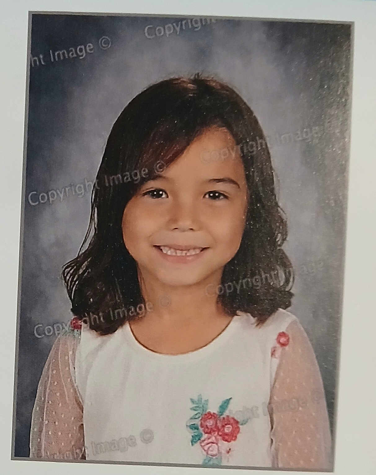 Vanessa is registered to the contest to win money with this photo: child, girl, portrait, smiling, school_photo, white_shirt, embroidered_flowers, dark_hair, shoulder_length_hair, polka_dot_sleeves, studio_background, face, person, child_portrait, cute, happy, casual_clothing, young, innocence, photography