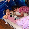 Vanessa is registered to the contest to win money with this photo: child, children, dog, pet, mattress, blanket, peace_sign, smile, cuddle, indoor, floor, wooden_floor, casual, pink_clothing, red_clothing, happy, playful, home, relaxed, portrait