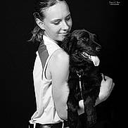 Ava participe au concours pour gagner de l'argent avec cette photo : affection, animal, black_and_white, casual_clothing, closeup, dark_background, dog, friendship, happy, hug, leash, pet, portrait, short_hair, sitting, sleeveless_top, smile, studio, woman, young_adult