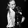 affection, animal, black_and_white, casual_clothing, closeup, dark_background, dog, friendship, happy, hug, leash, pet, portrait, short_hair, sitting, sleeveless_top, smile, studio, woman, young_adult