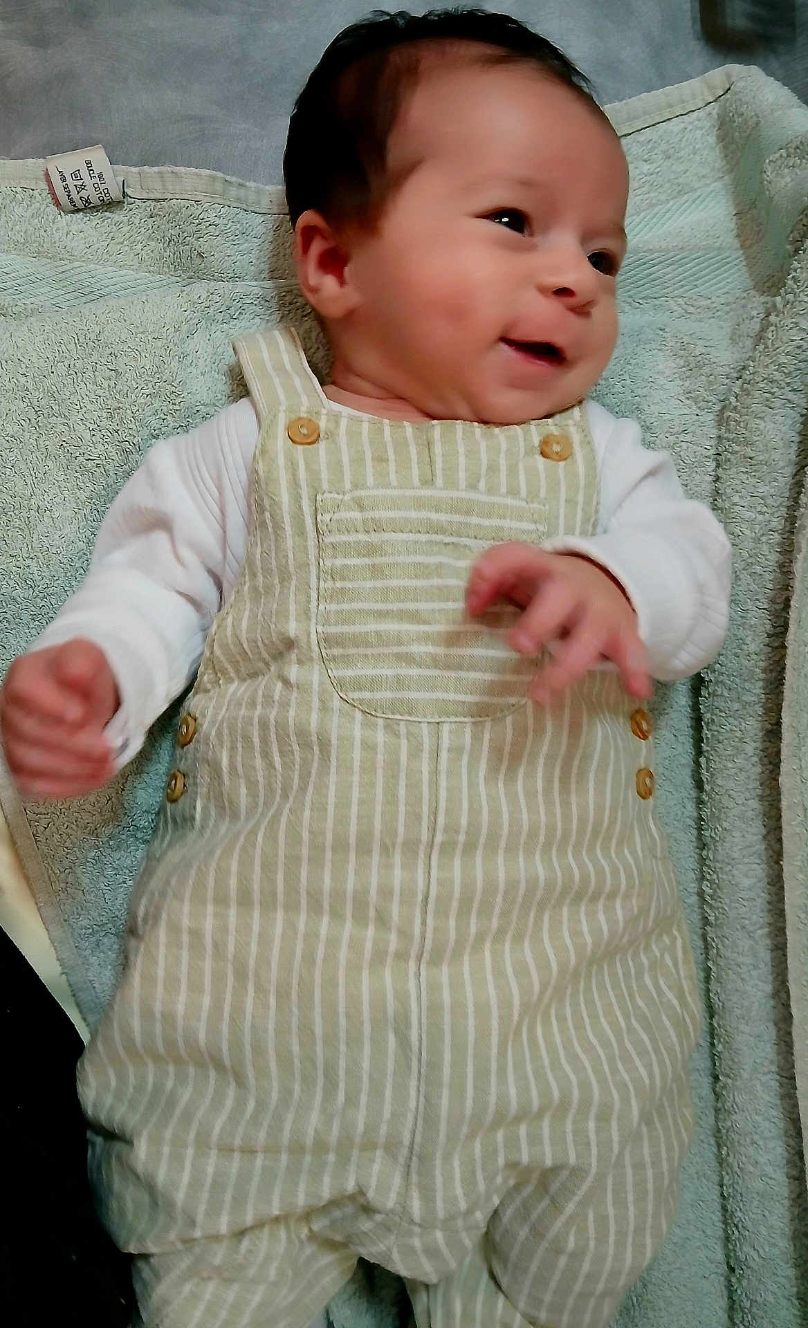 Malek participe au concours pour gagner de l'argent avec cette photo : baby, infant, smiling, overalls, striped_clothing, white_shirt, towel, laying_down, happy, face, hands, cute, child, portrait, young, indoors, soft_texture, fabric, skin, person