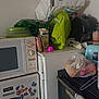 appliance, bags, cat_paw, clutter, container, corner, countertop, food_storage, fridge, green_bag, household, juice_carton, kitchen, microwave, miscellaneous, oven, plastic_bag, sticker, towel, wall