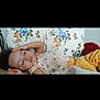 child, toddler, sleeping, couch, floral_cushions, indoor, relaxation, yellow_pants, patterned_shirt, curly_hair, peaceful, resting, person, home, cozy, portrait, casual_clothing, soft_lighting, cute, young