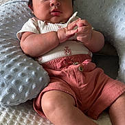 Noah is registered to the contest to win money with this photo: baby, infant, cap, pink_clothing, shorts, pillow, bed, blanket, texture, hands, face, curious, cute, child, indoors, soft_lighting, skin, portrait, sitting, cozy